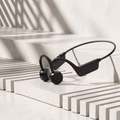 Black bone conduction wireless earplugs resting on a modern, minimalist white marble staircase with dramatic diagonal shadows.