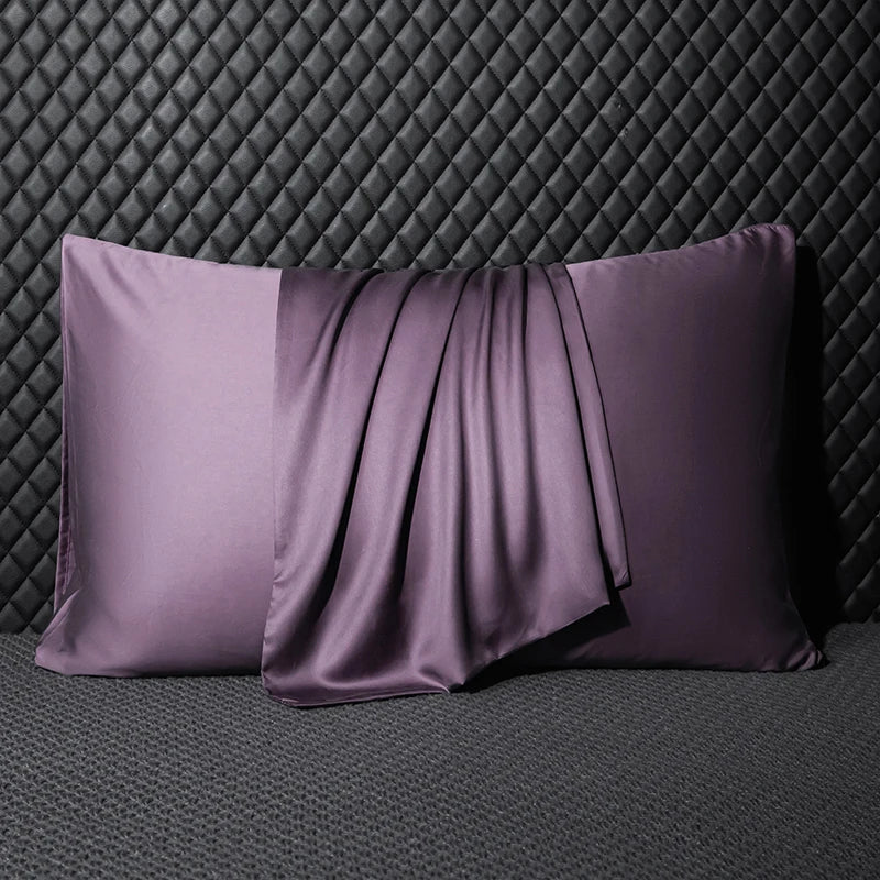 Two purple satin pillows on a textured gray surface with a dark quilted wall background.