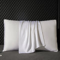 Two white pillows with a white towel draped over them against a dark textured wall.