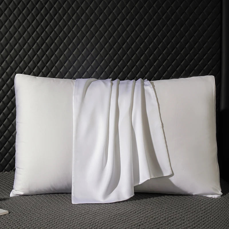 Two white pillows with a white towel draped over them against a dark textured wall.