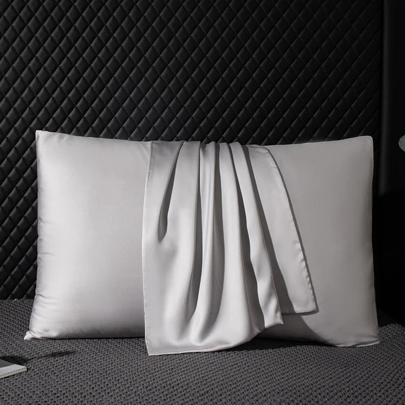 Two gray pillows with a folded gray fabric on a textured black surface.