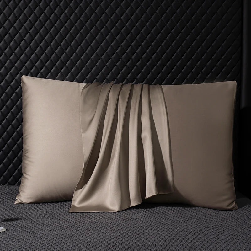 Two beige satin pillows on a textured dark surface with a geometric pattern.