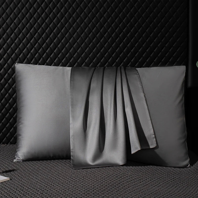 Two gray satin pillows on a textured black surface with a geometric patterned wall in the background.