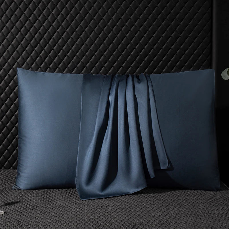 Two blue satin pillows on a textured black surface with a dark quilted headboard.